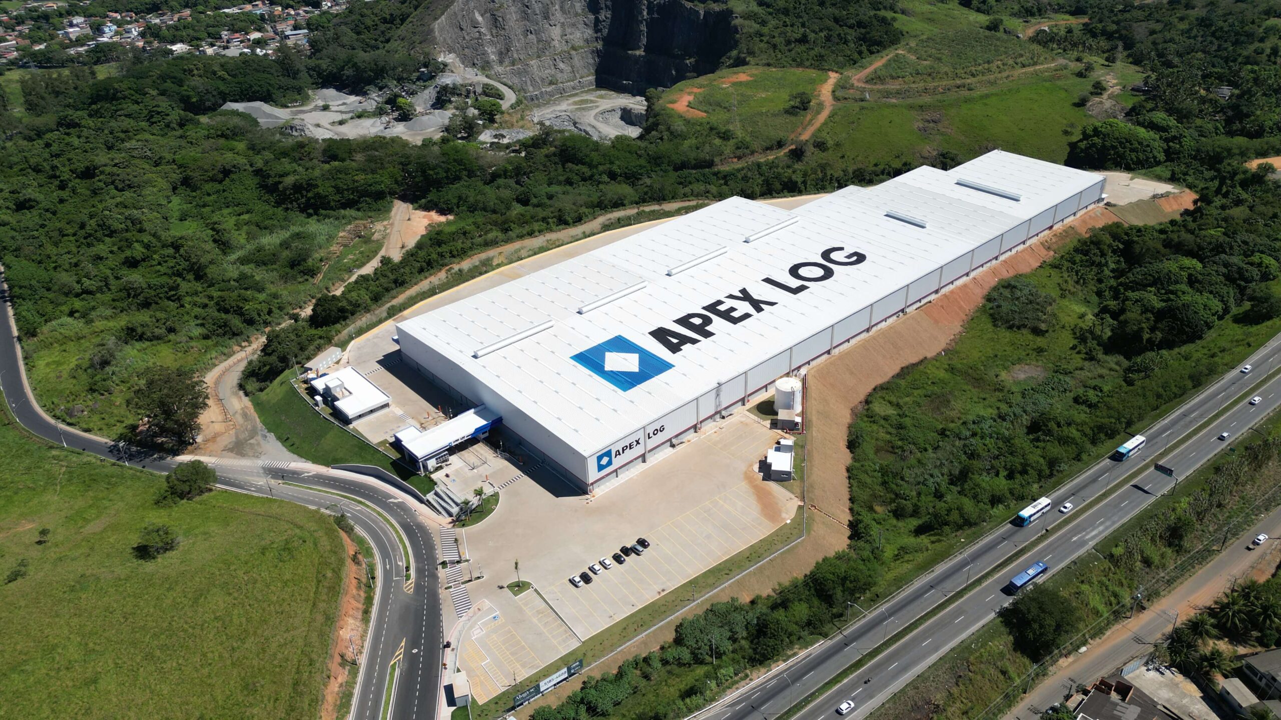 Foto aérea do Centro de Distribuição Apex Log Pitanga, localizado na Serra, Espírito Santo, próximo a uma rodovia e cercado por áreas verdes.