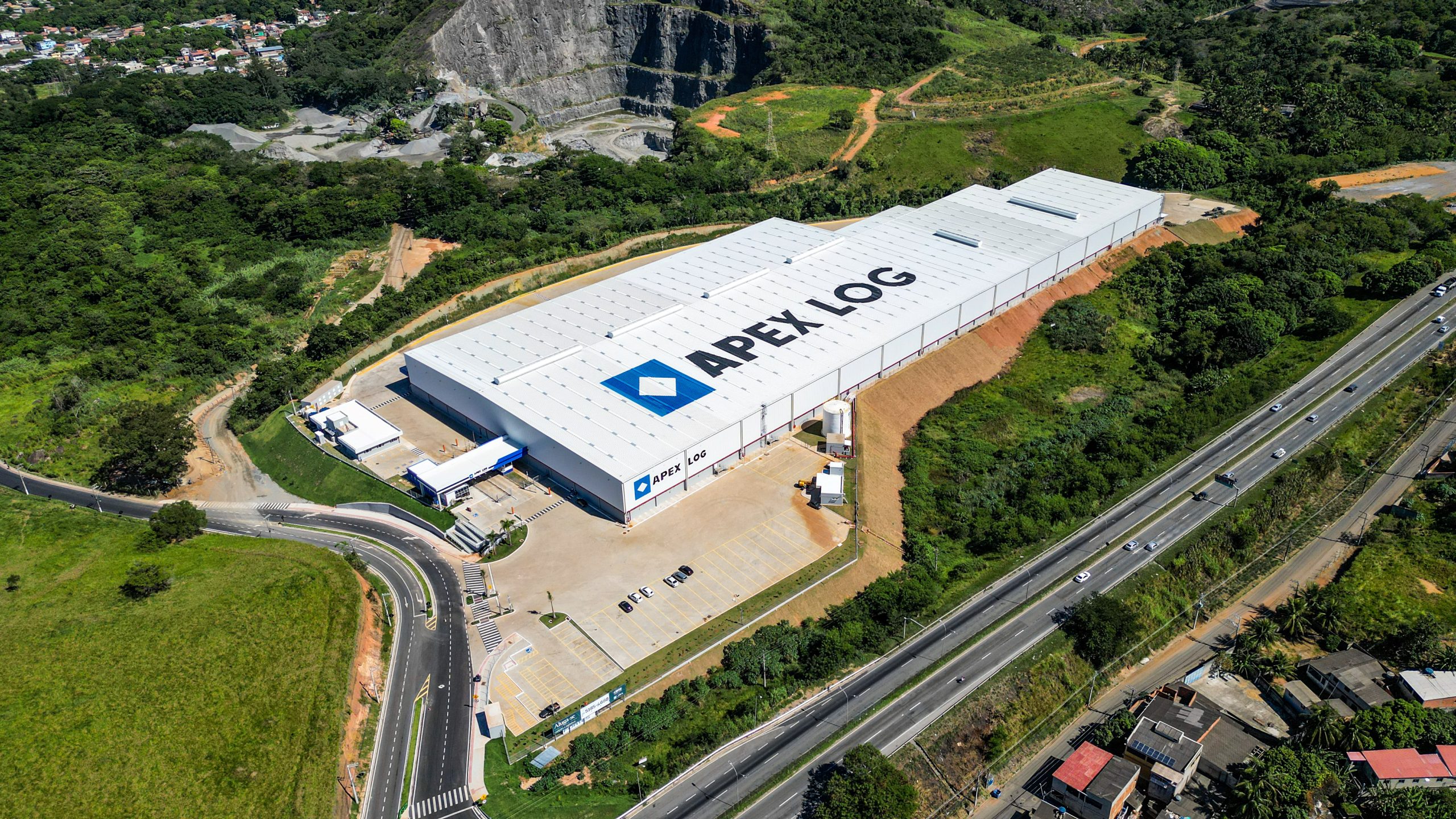 Vista aérea do galpão logístico da Apex Partners na Serra (ES), projetado em meio à vegetação com acesso direto à rodovia.