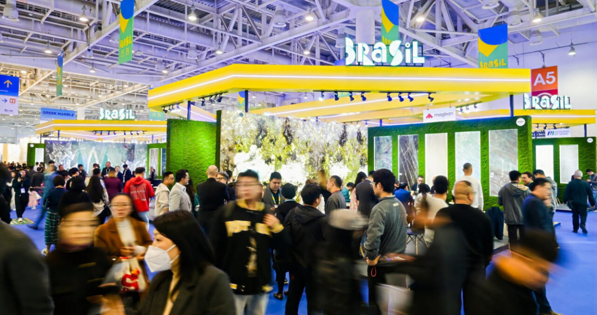Panorâmica do pavilhão Brasil na Xiamen Stone Fair 2025 com painéis de mármore e granito e público circulando